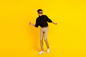 Fototapeta na wymiar Full size photo of optimistic nice brunet guy dance wear spectacles black sweater trousers sneakers isolated on yellow background