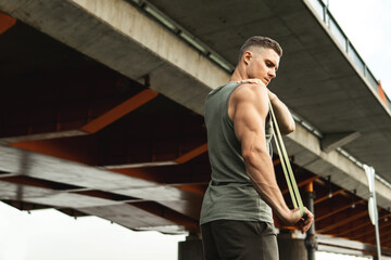 Muscular man during workout with a resistance rubber band on a street.