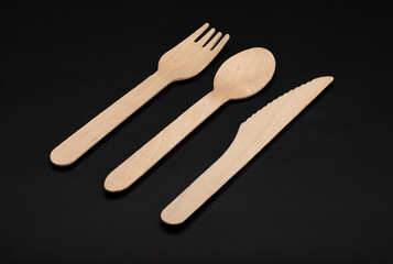 Wooden spoon and fork with knives  , disposable tableware on black background. Eco-friendly materials