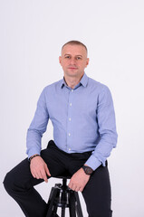 Naklejka premium A man in a blue shirt and black trousers sits on a stool on a white background