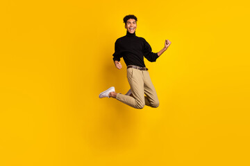 Fototapeta na wymiar Photo of funny lucky dark skin guy dressed black pullover jumping rising fists isolated yellow color background