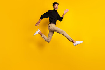 Naklejka na ściany i meble Photo of pretty charming dark skin man wear black sweater eyewear running fast jumping isolated yellow color background