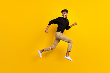 Photo of funky sweet dark skin man wear black sweater jumping running looking back empty space isolated yellow color background