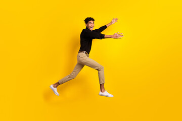 Fototapeta na wymiar Photo of funny charming dark skin guy dressed black pullover jumping running open arms isolated yellow color background