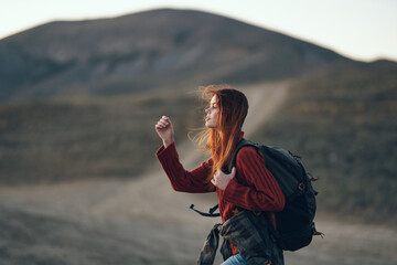 a traveler in a sweater with a backpack on her back looks to the side outdoors in the mountains