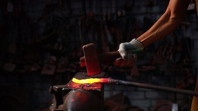 slow motion close up hand with the hammer of blacksmith man forges a metal product in dark indoors studio