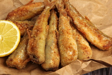 fried breaded fish served on paper, decorated with fresh lemon, old wood background. horizontal view from above 