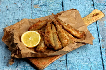 fried breaded fish served on paper, decorated with fresh lemon, old wood background. horizontal...