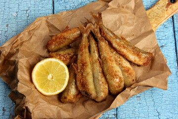 fried breaded fish served on paper, decorated with fresh lemon, old wood background. horizontal view from above 