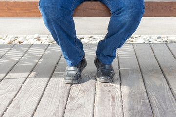 a man sits on a bench in the day. the legs are in the frame only