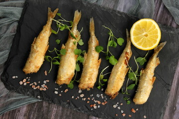 fried breaded fish served on a black stone, decorated with fresh lemon, dark wooden background....