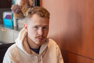 a man about 30 in a hoodie with a red mustache sits in a cafe