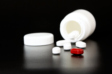 A white bottle with a lid and scattered white and red tablets on a black background