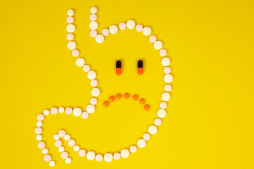 A stomach of pills with a sad face on a yellow background. Gastritis, stomach and digestive problems.