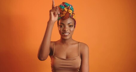African woman with bright makeup points index finger up. The girl smiles at the camera.