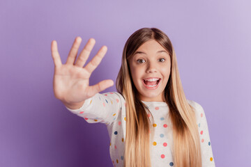 Attractive lovely cheerful pre-teen girl showing you high five isolated over purple background