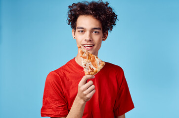 man holding a slice of pizza in his hand and curly hair red t-shirt blue background