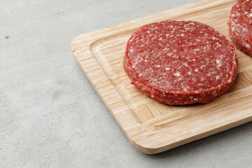Raw beef burger patty on wooden board