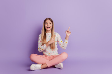 Cool little lady sit floor point finger empty space on purple background