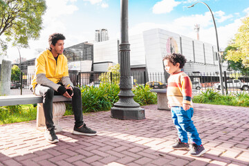 young black latino man, dressed in yellow, sitting in an urban plaza, with his son, father's day concept