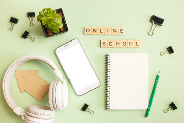 Office workspace background. Smartphone, headphones, and notepad on green pastel background. Online school or distance education concept. Mock up for phone apps.