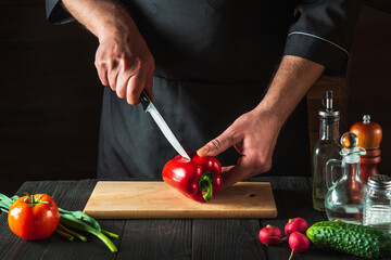 Professional chef or cook is cutting red peppers for salad on a restaurant kitchen table. Vegetable diet or snack idea