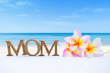 Fotobehang Mother's day card background idea, plumeria flower and mom wooden font over blurred beach background © sirirak