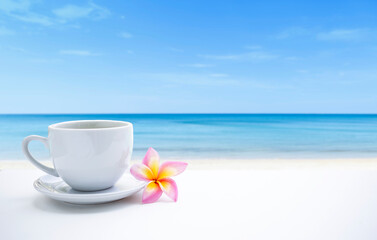 White coffee cup and plumeria flower on the beach, relaxing by the sea, summer holiday, vacation time, outdoor day light