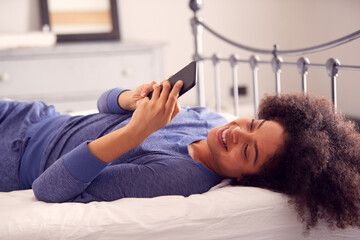 Woman Lying On Bed With Mobile Phone Wearing Pyjamas
