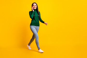 Full size profile side photo of young happy positive girl go walk talking on phone isolated on yellow color background