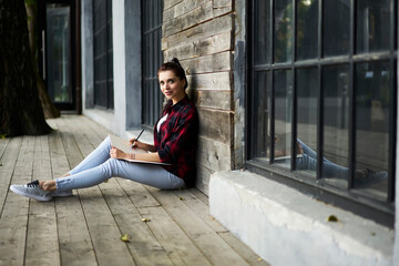 Portrait of Caucasian female student with education sketchbook for learning knowledge information posing outdoors, young hipster girl holding textbook for doing homework and looking at camera