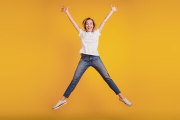 Fototapeta na wymiar Smiling positive girl jumping on yellow background raise hands