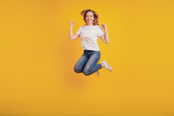 Fototapeta na wymiar Smiling positive girl jumping active cheerful mood on yellow background