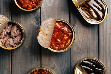 Top view of opened cans with fish conserves on wooden background
