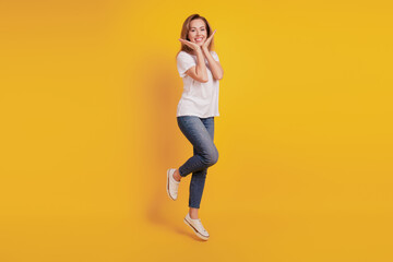 Fototapeta na wymiar Smiling positive girl jumping on yellow background palms face toothy smile
