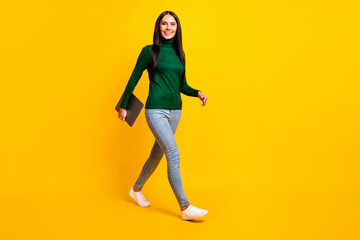 Fototapeta na wymiar Full body photo of charming nice young woman walk empty space good mood hold computer isolated on yellow color background