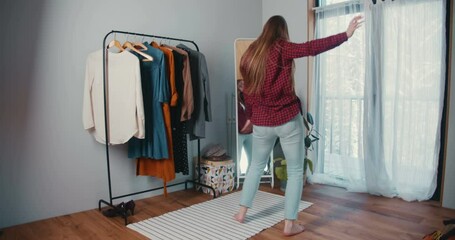 Happy beautiful young Caucasian blonde woman dancing, having fun at mirror feeling confident in cozy clothes room.