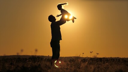 Silhouette dad throws happy little daughter into the sunset sky. Father's day. The child wants to fly above the ground. A parent with a child plays at dawn. Family and childhood concept. Kid jumps on