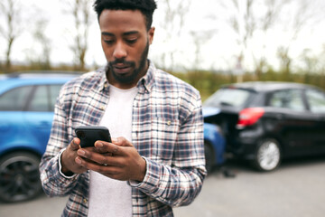 Young Male Driver Calling Car Insurance Company On Mobile Phone After Road Traffic Accident