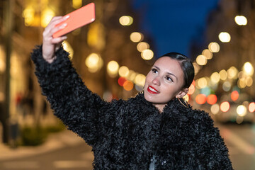 pretty Young Caucasian woman taking a selfie with smartphone at night with lights