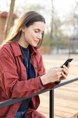 Cheerful young woman looking in her mobile phone with a cute smile otdoors in the park