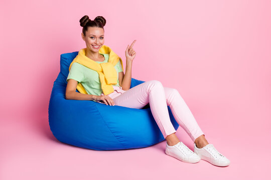 Full Size Photo Of Happy Woman Point Empty Space Sit Chair Wear Pink Pants Green T-shirt Tight Jumper Isolated On Pastel Color Background