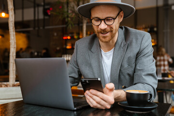 White bearded man using laptop and cellphone in cafe outdoors