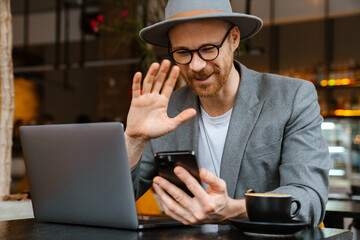 White bearded man using laptop and cellphone in cafe outdoors