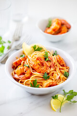 Spaghetti with shrimps or prawns garnished ith lemon and parsley leaves in a white bowl