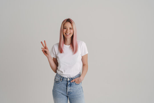 Young woman with pink hair smiling and gesturing peace sign