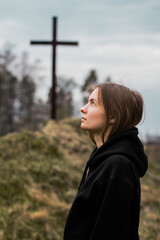 The girl looks into the sky against the background of the cross. Faith in God. Hope in God