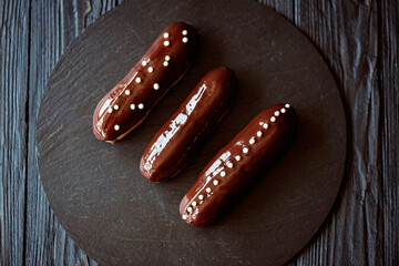 French dessert eclairs or profiteroles with dark chocolate glaze and drops. Pastry cakes with cream and topping. Soft selective focus.