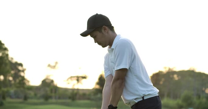 Asian male golfer holding driver watching his ball after teeing off on fairway in slow motion.