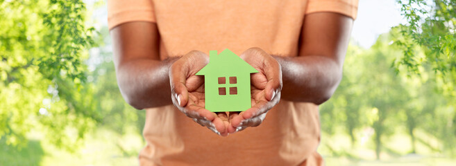 eco living, environment and sustainability concept - close up of young african american man holding green house icon over natural background